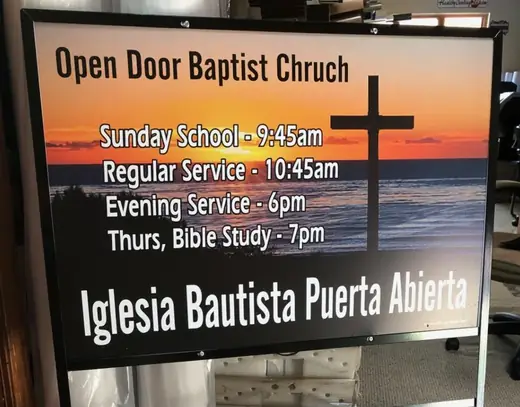 Open-door church service-times sign mounted on a building
